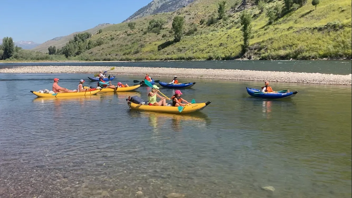 Kayakers and paddleboarders on the Snake River with mountain backdrop in Jackson Hole