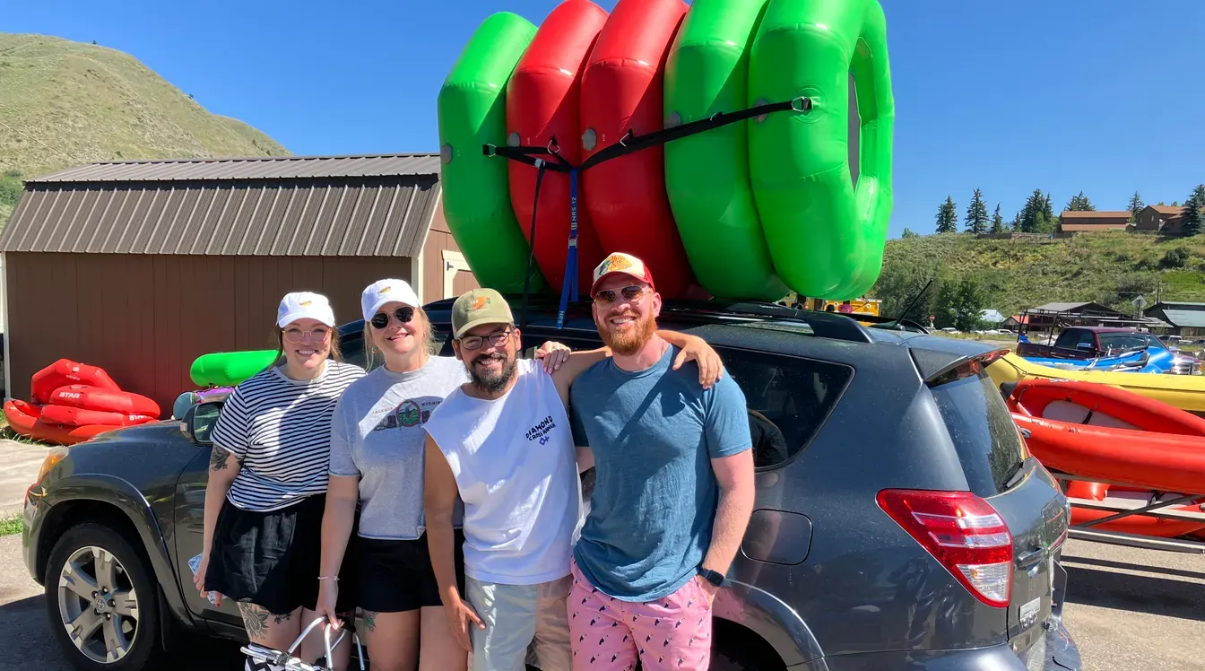Happy group of four with inflatable kayak loaded on SUV ready for Snake River adventure